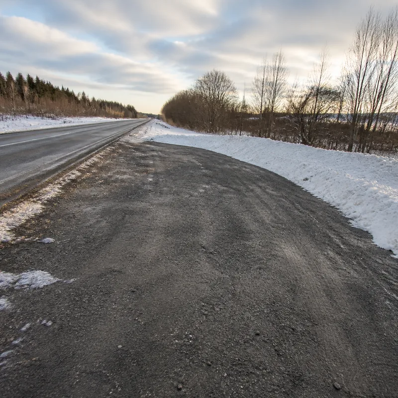 A freshly ploughed pull off bay beside a straight rural road in winter, clear and completely empty, with snow banked along its outer edge.