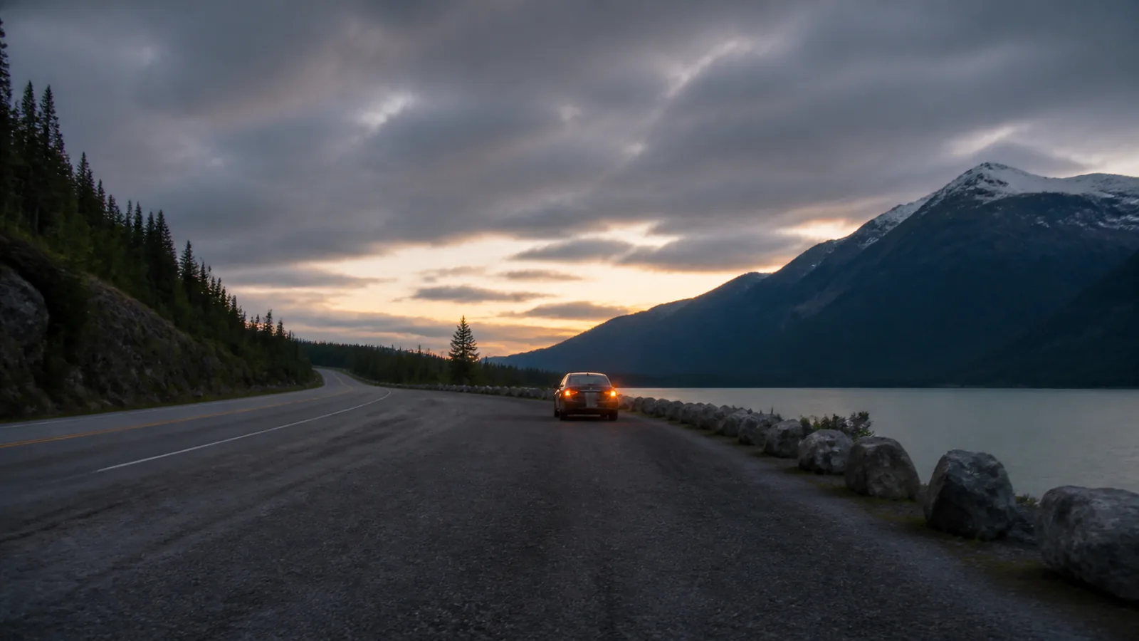 A quiet pull off bay at dusk with a stopped car showing its hazard lights, seen from far enough behind that no detail of the vehicle reads.
