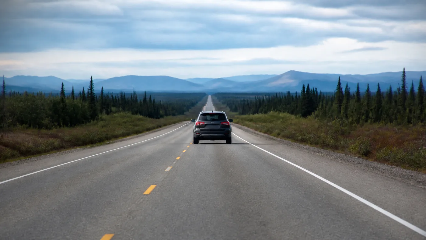A two lane rural highway on a long open straight with a broken centre line, one slow vehicle ahead and clear road beyond it.